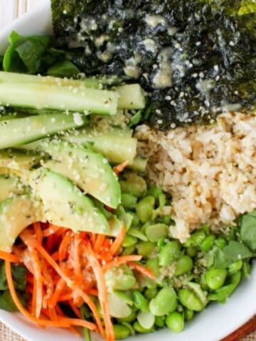 Vegetarian sushi salad bowl with rice, edamame, avocado, veggies, and miso dressing.