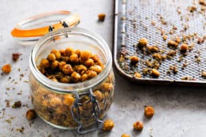 Vegan cheesy herb roasted chickpeas in mason jar next to baking pan.