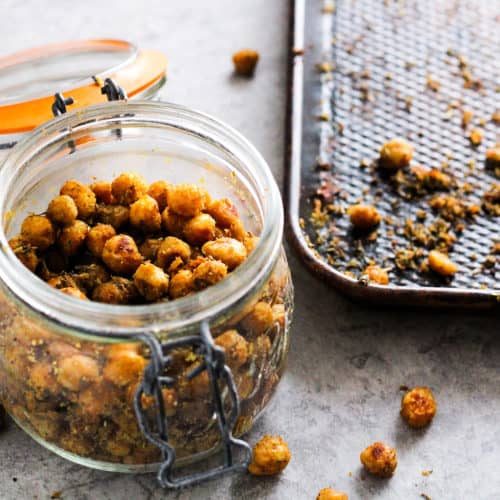 Vegan cheesy herb roasted chickpeas in mason jar next to baking pan.