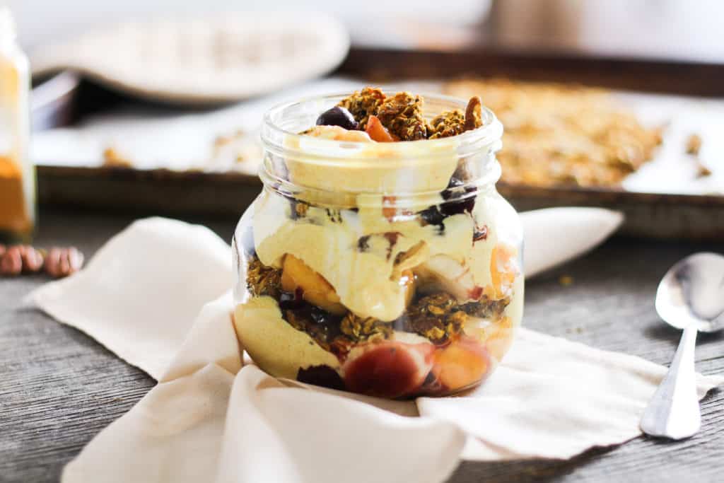 golden milk granola parfait in a mason jar with pan of granola in the background