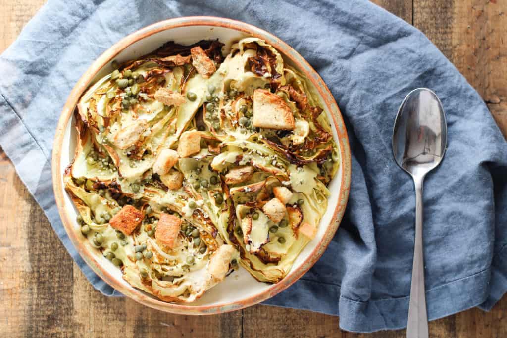 Overhead view of Vegan Roasted Cabbage Caesar Salad with blue napkin against wood backdrop.