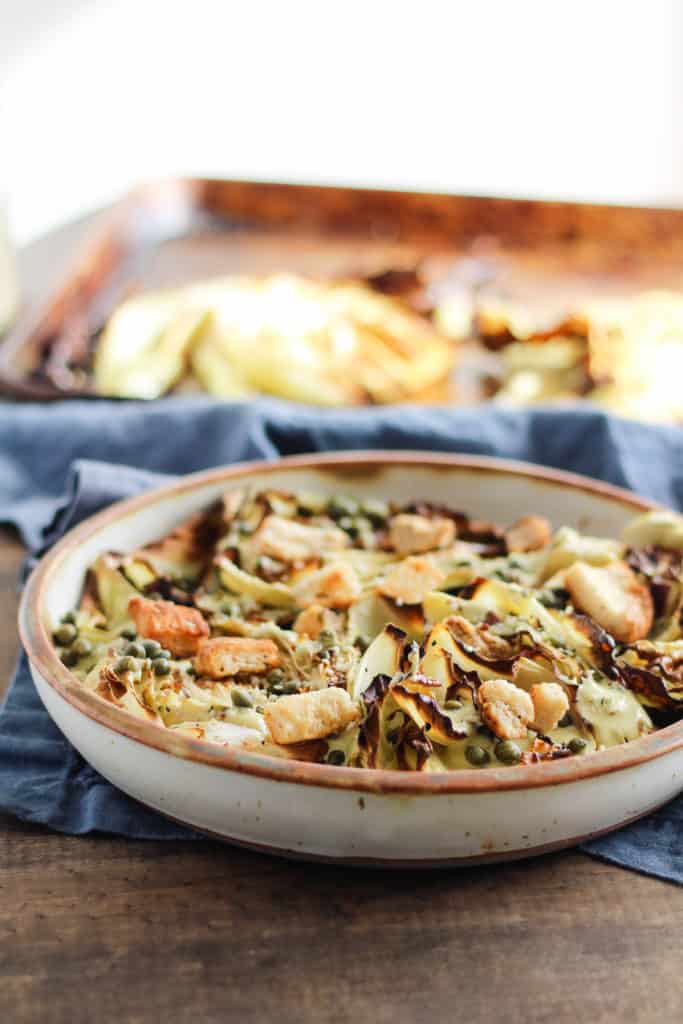 Vegan Roasted Cabbage Caesar Salad in cream stone dish with baking pan in background.