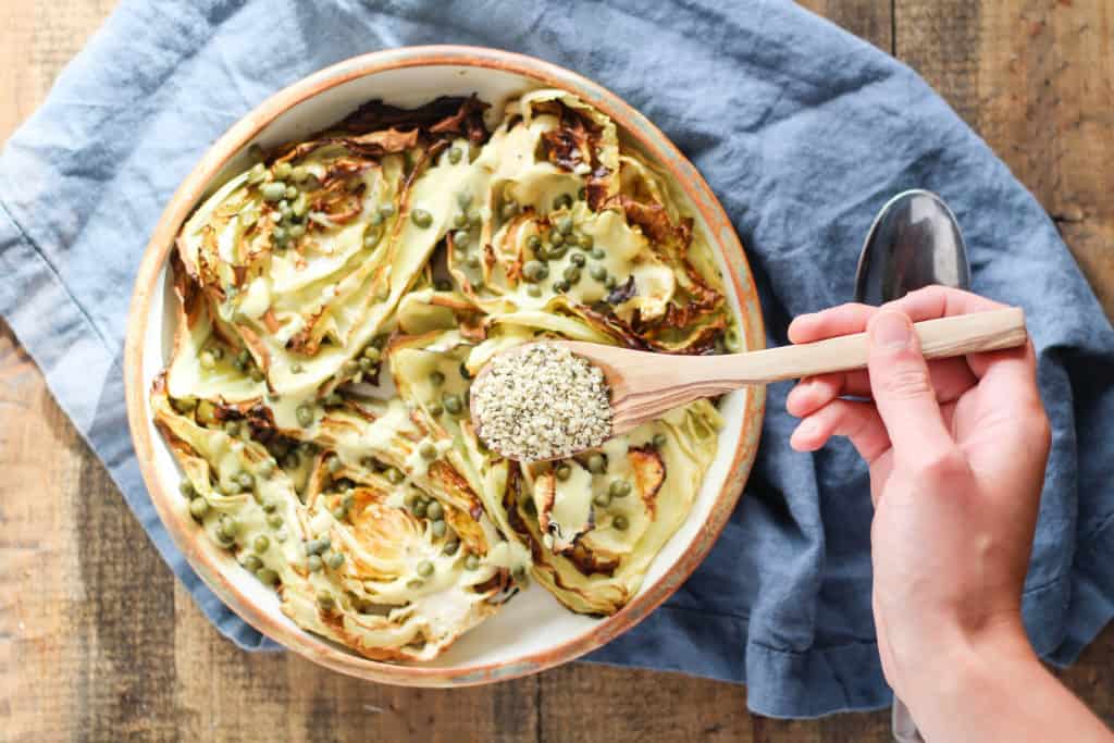 Overhead view of roasted cabbage Caesar salad with spoonful of hemp seeds being poured on top.