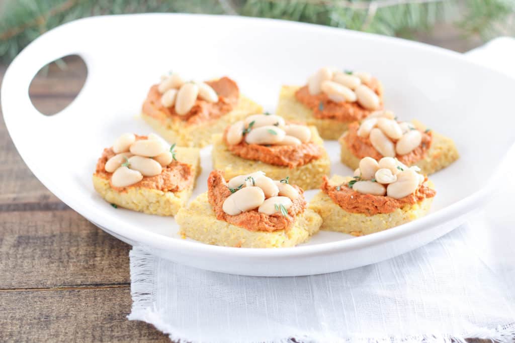 Cannellini Bean Polenta Squares are a festive (and completely vegan) appetizer for the holidays and beyond. Guests will love this delicious bite of polenta (Italian grits) smothered in roasted red pepper and sun-dried tomato bean and walnut spread. 