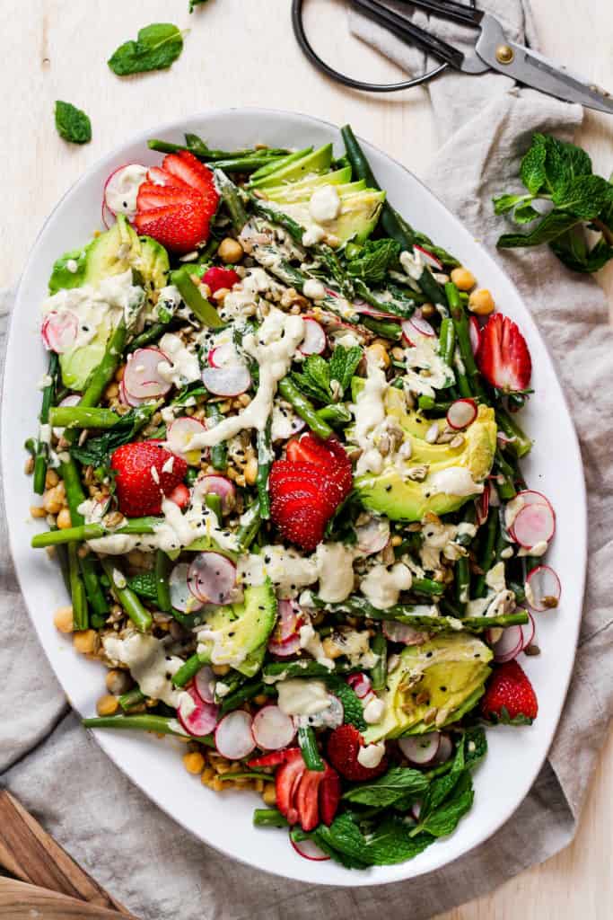 Spring salad with tahini dressing on a white platter.