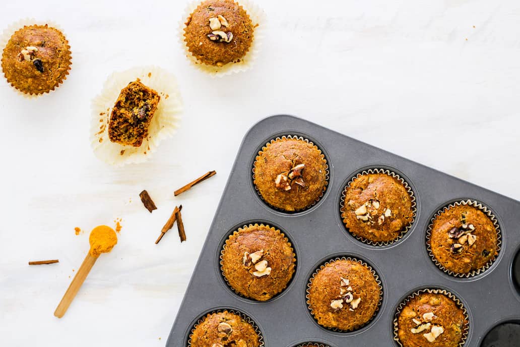 Overhead shot of gluten-free muffins in a muffin tin with spoonful of turmeric against shite backdrop.