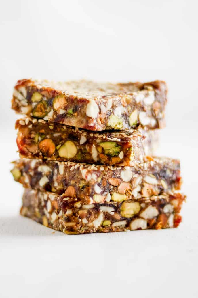 Stack of sesame date bars with pistachios against white backdrop.