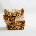 Stack of four sesame date bars with pistachios with white background.