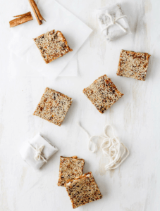 Sesame date bars arranged on a white backdrop. Wrapped in parchment paper and tied with string.