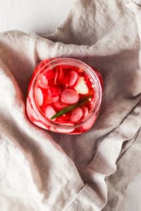 Overhead shot of quick-pickled radishes in a mason jar with natural linen napkin.