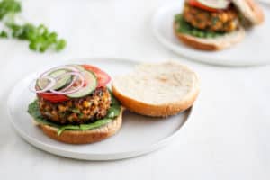 Moroccan Chickpea Burger on a bun with tomato, onion, and cucumber on white backdrop.