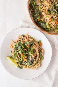 Peanut noodles with edamame and spinach on white plate with basil.