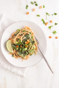 Peanut noodles with edamame and spinach on white plate with basil and peanut garnish.