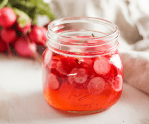 Quick pickled radishes in mason jar with bunch of radishes in background.