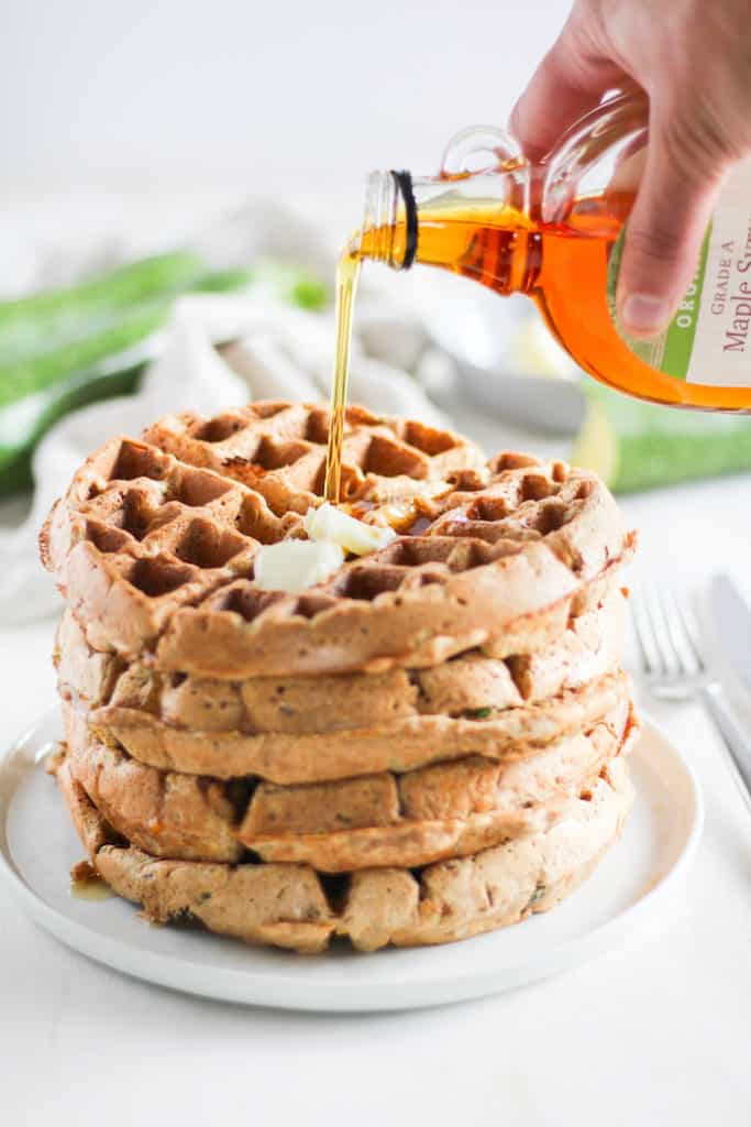 Stack of whole wheat zucchini bread waffles action shot with maple syrup being poured on top.