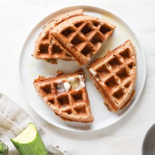 Overhead shot of sliced whole wheat zucchini bread waffles on white plate.