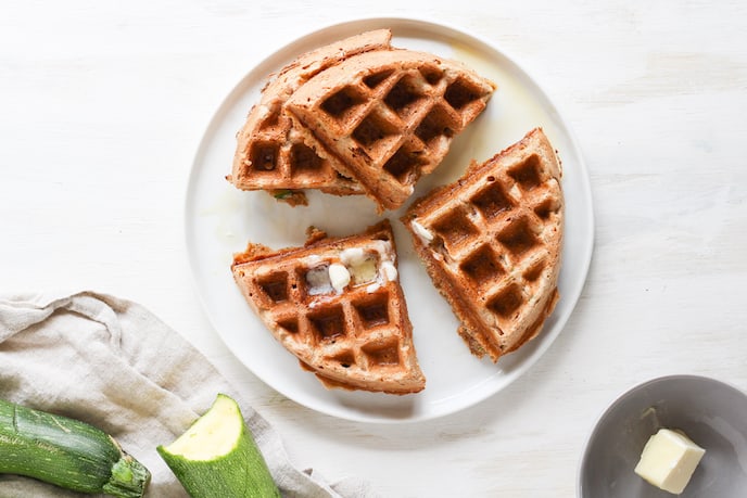 Overhead shot of sliced whole wheat zucchini bread waffles on white plate. 