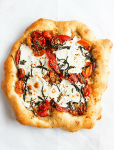 Homemade pizza with caprese toppings against white backdrop.