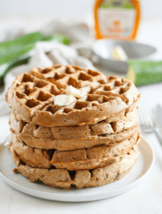Stack of whole wheat zucchini bread waffles topped with butter on a white plate.