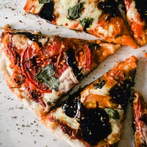 Slices of caprese pizza with sliced heirloom tomato, basil, fresh mozzarella, and balsamic glaze.