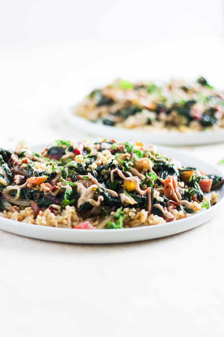 straigt-on shot of toasted freekeh with rainbow chard and tahini sauce on white plate against white background.
