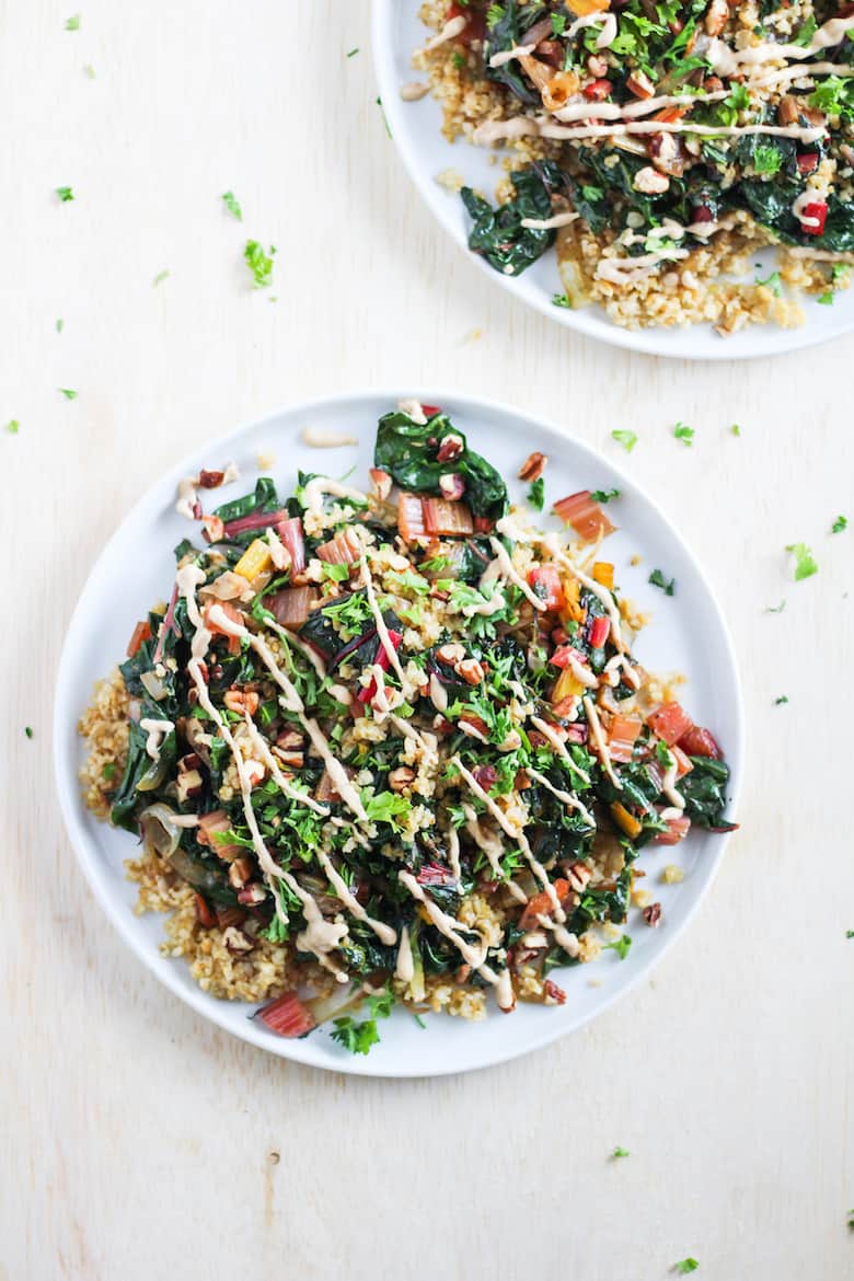 Toasted freekeh with rainbow chard and tahini sauce on white plate against white background.