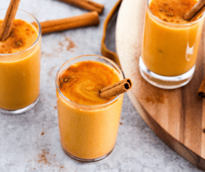 Pumpkin lassi drinks in small glasses with cinnamon stick garnish.