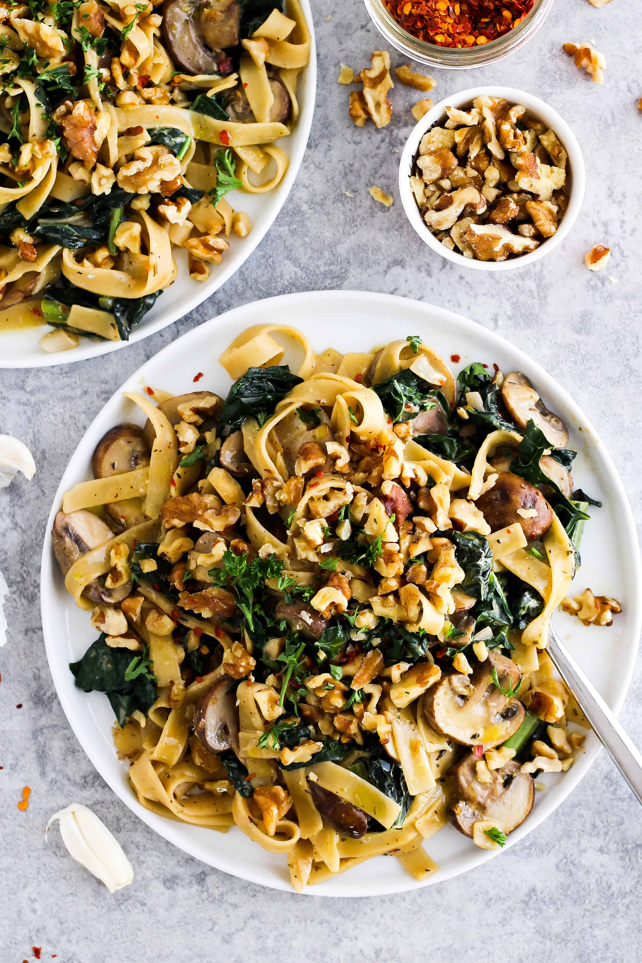 Creamy vegan pasta on white plate with walnuts and crushed red pepper.