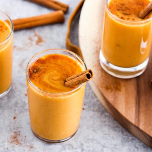 Pumplin lassi drinks with cinnamon stick garnish on wood board.