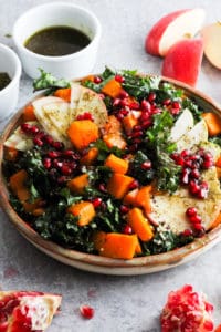Harvest Zaatar Kale Salad in stone dish with ramekin of dressing and fruit around plate.
