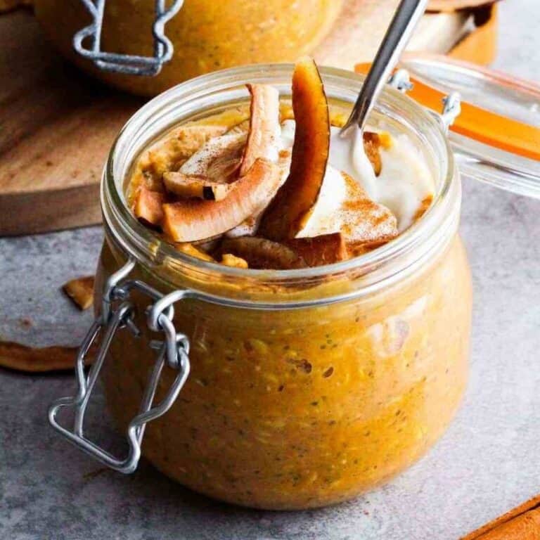 Pumpkin overnight oats in a glass jar with coconut strips and coconut cream garnish.