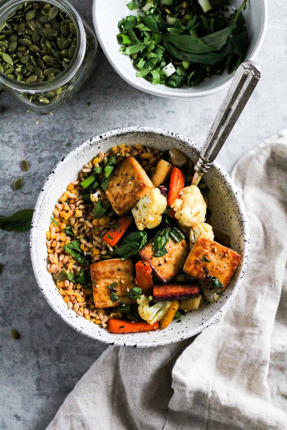 Sheet pan tofu bowls in white stone bowl with linen napkin and grey background.