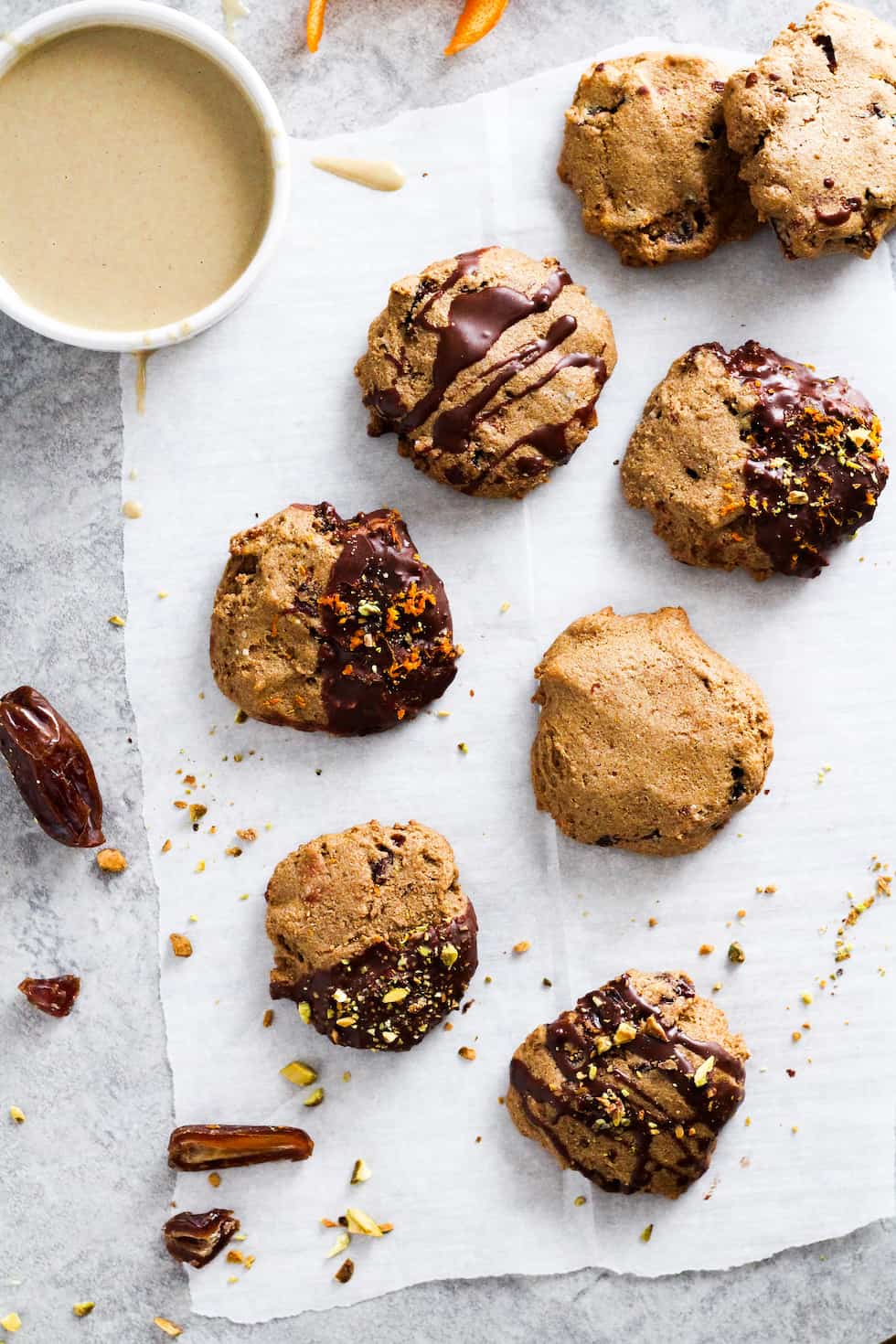Tahini cookies on parchment paper. Some cookies are dipped in chocolate. Small bowl of tahini in corner.