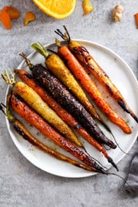 Roasted rainbow carrots on white plate with orange and ginger around the edges.