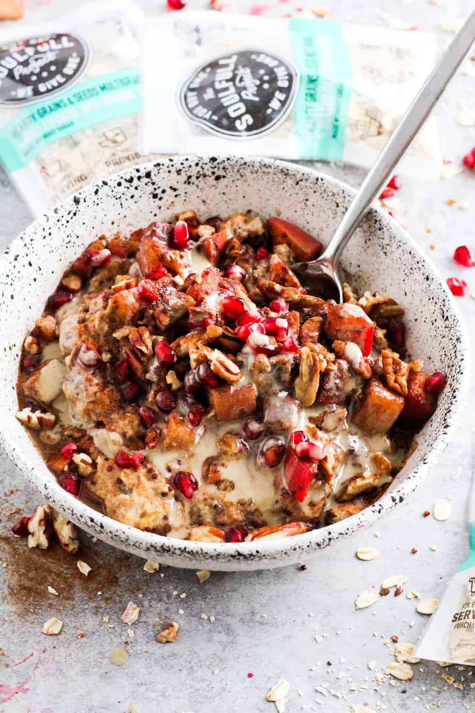 Cinnamon apple tahini oatmeal bowl in white stone bowl with packets opf The Soulfull Project cereal in the background.