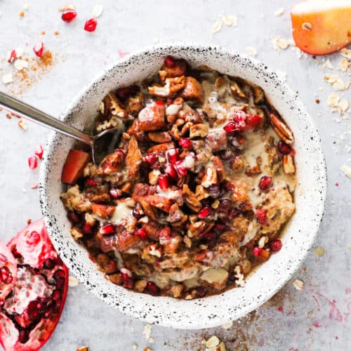 Cinnamon apple tahini oatmeal bowl in white stone bowl with pomegranate and apple.