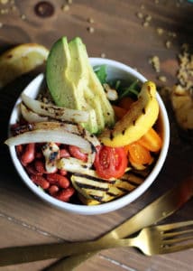 Bowl recipes. Overhead shot of vegetarian bowl with avocado against wood background with gold silverware.