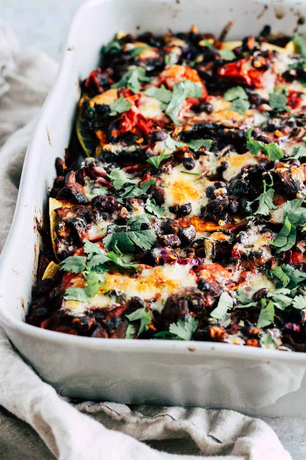 Close up view of black bean taco bake in grey ceramic baking dish with cream linen napkin.