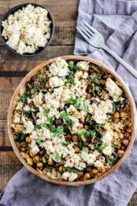 Bowl recipes. Greek roasted chickpeas with tofu feta in brown ceramic dish iwth blue napkin and wood background.