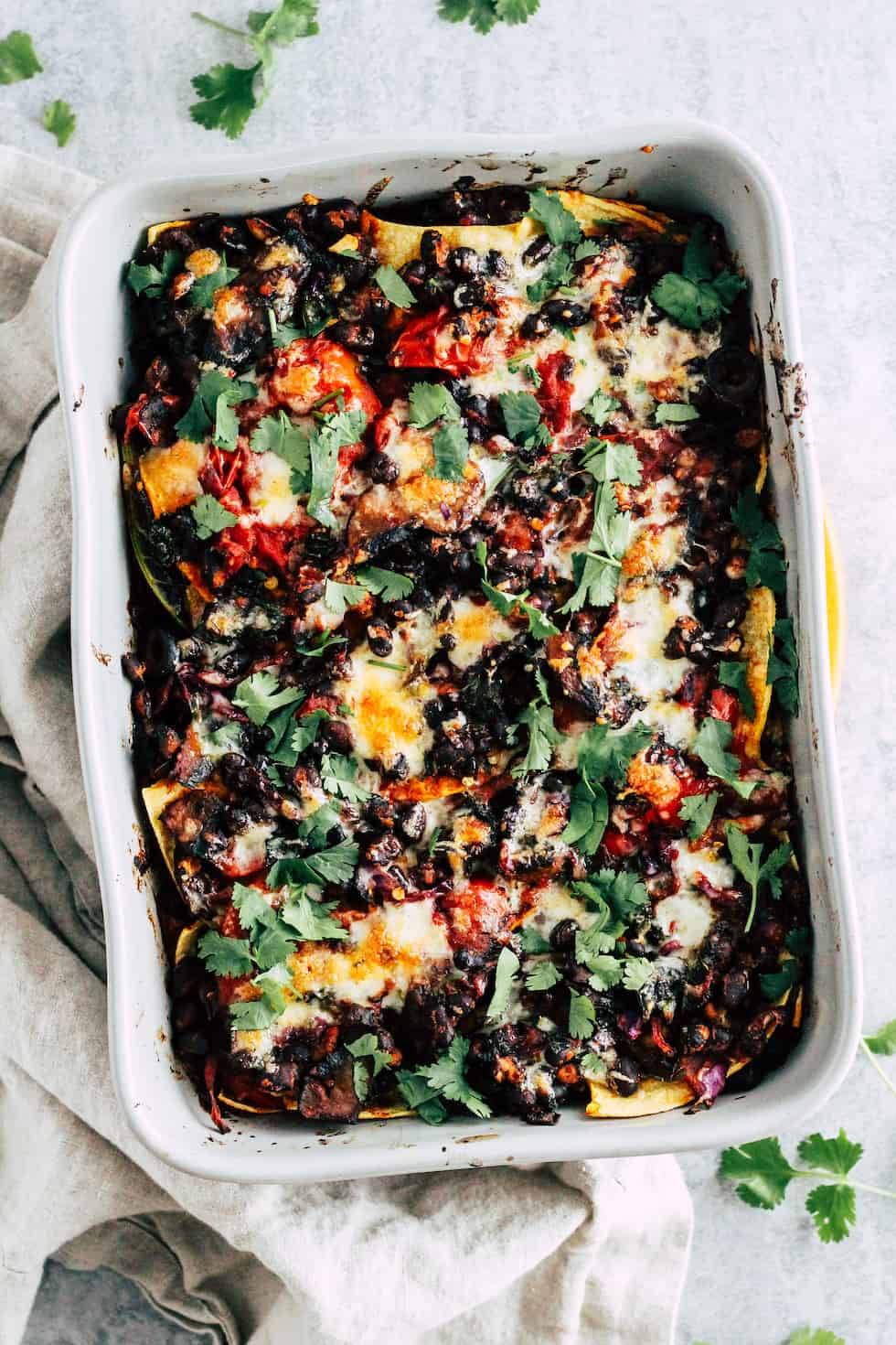 Overhead shot of black bean taco bake in grey ceramic baking dish with cilantro around edges.