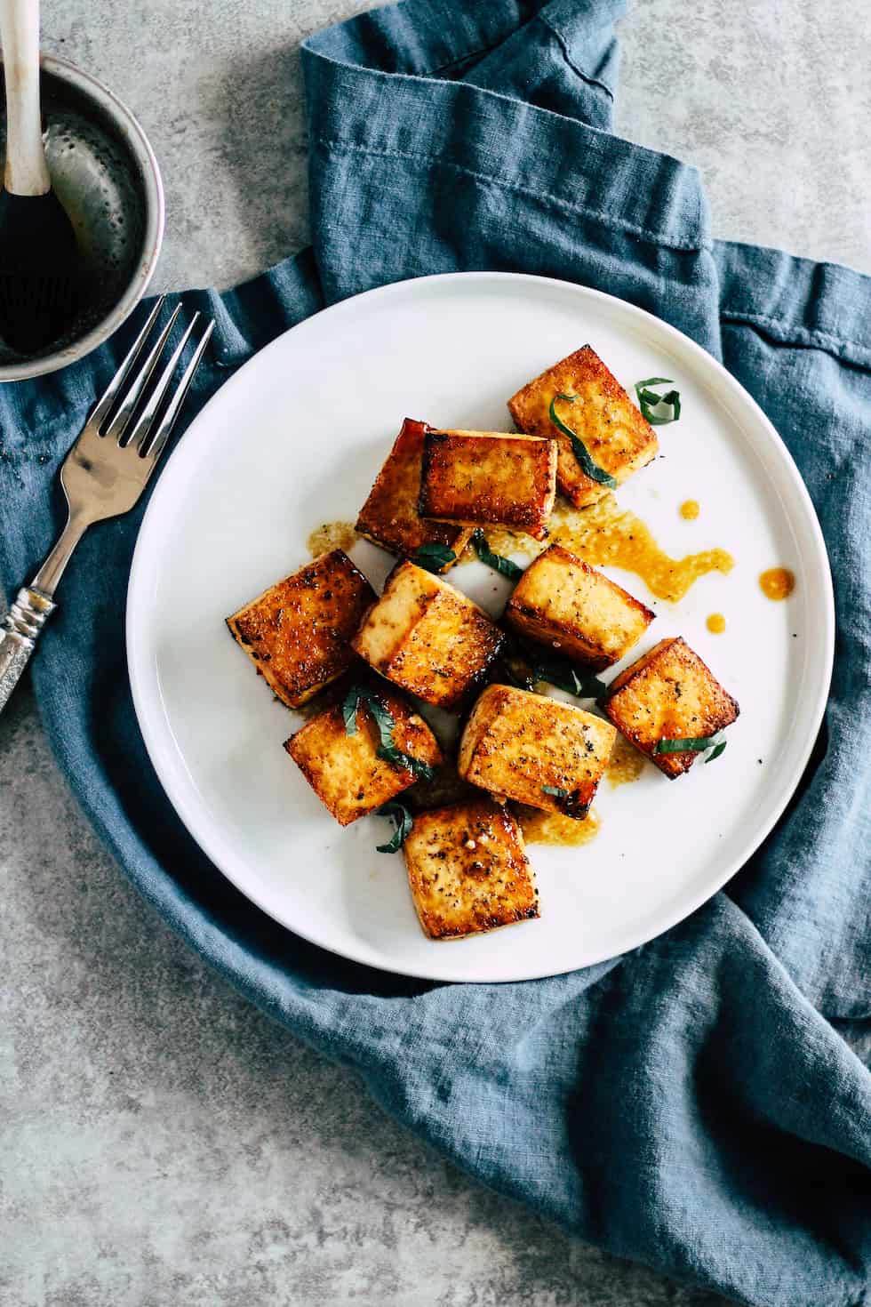 Crispy tofu on white plate with blue linen napkin against grey background.