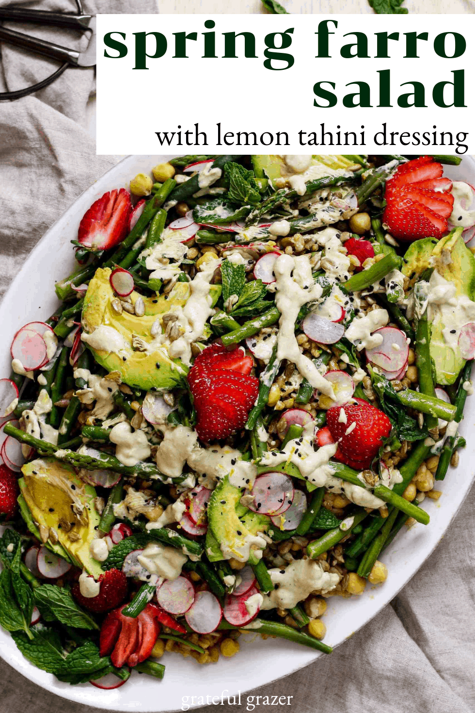 Title reads "spring farro salad with lemon tahini dressing." Green salad with avocado, grain, and strawberries on white platter with cream napkin.