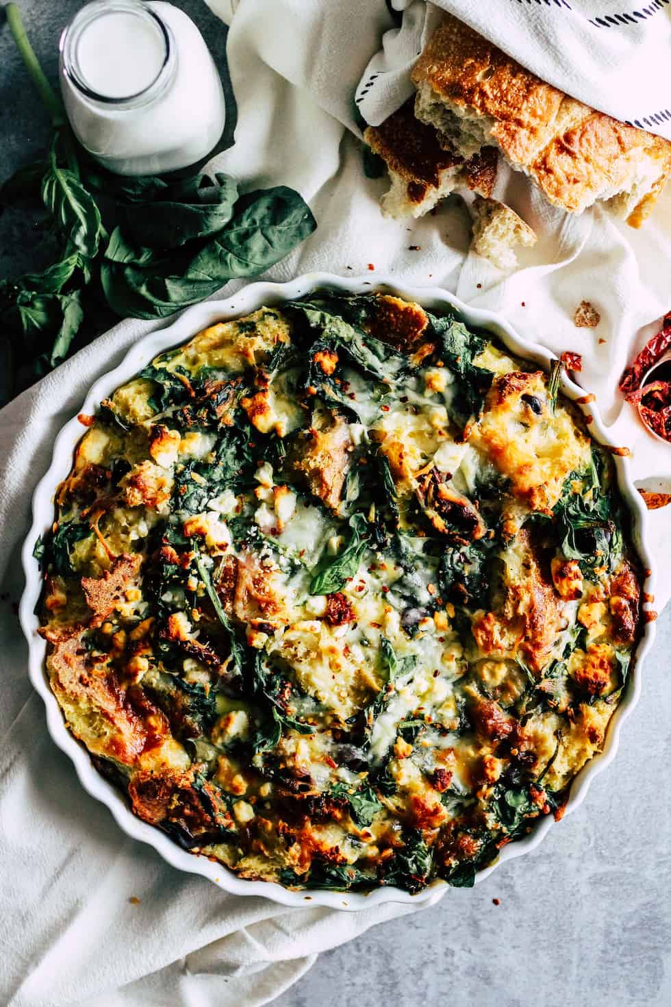 Tomato Basil Strata in white pie dish with jar of milk and loaf of bread.