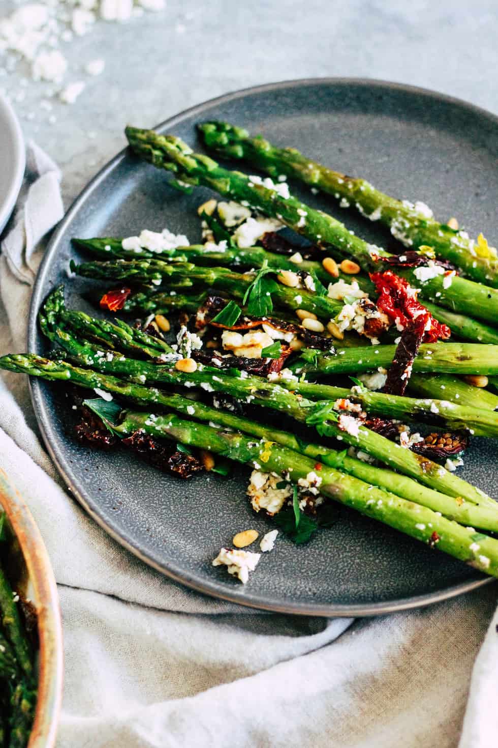 Asparagus spears on a gray plate with sun-dried tomato and feta cheese. 