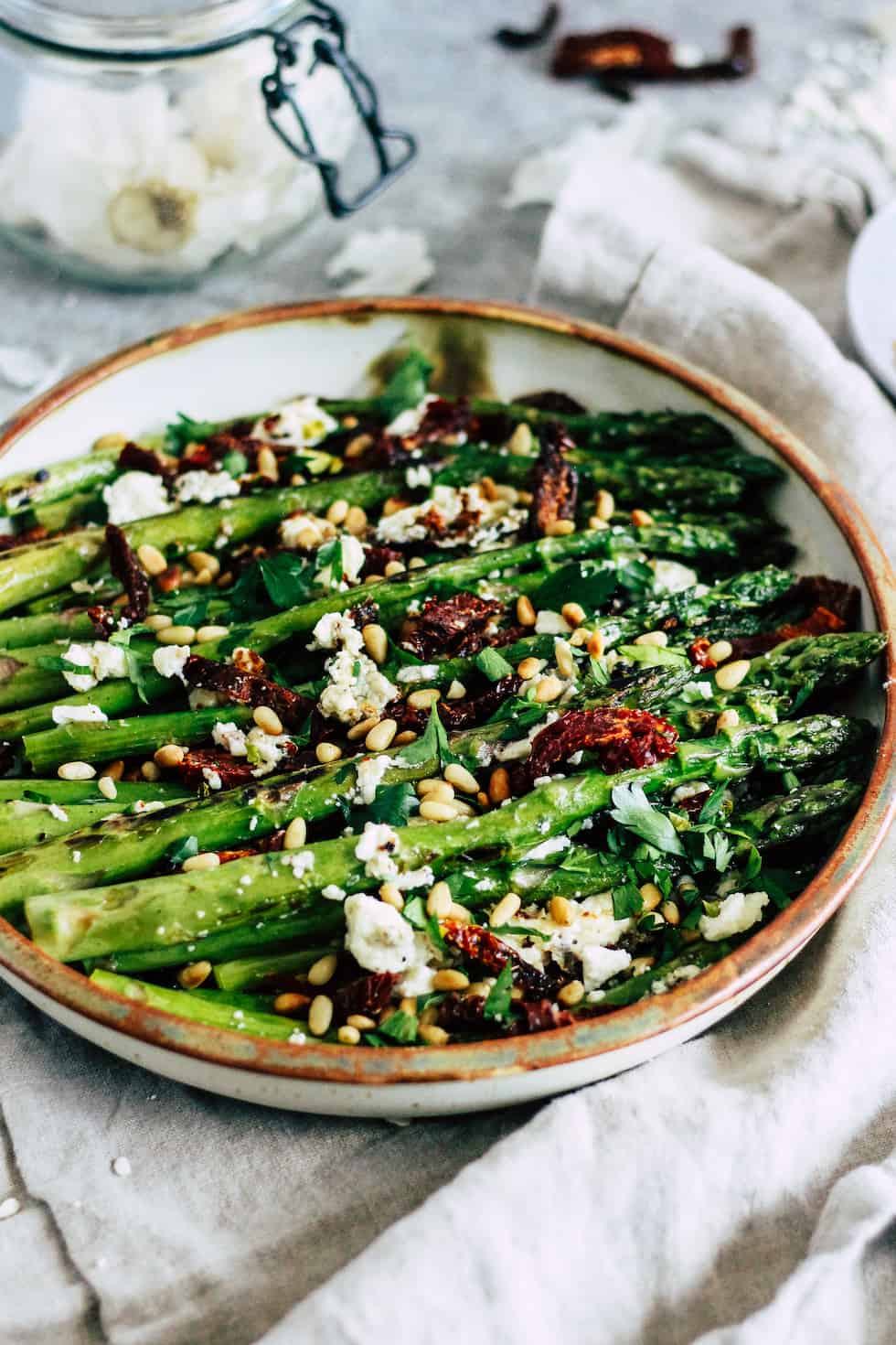 Pan roasted asparagus on ceramic dish with jar of garlic behind it. 