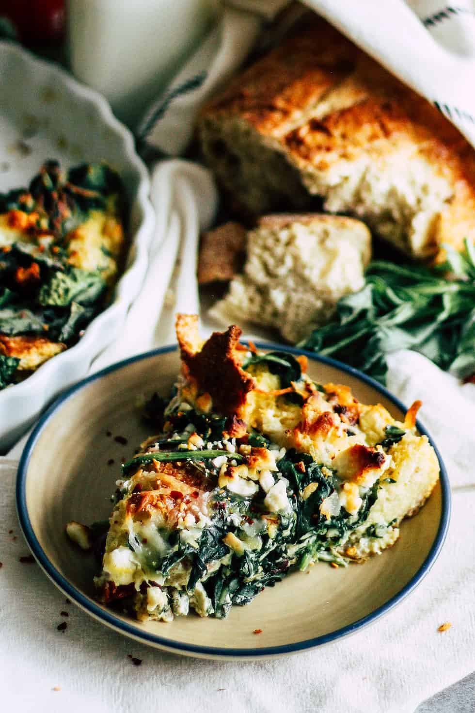 Slice of tomato basil strata on tan dish with loaf of bread in the background.