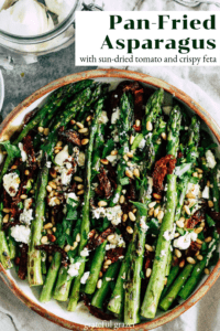 Asparagus in ceramic dish with title text that reads, "Pan-Fried Asparagus with Sun-Dried Tomato and Crispy Feta"