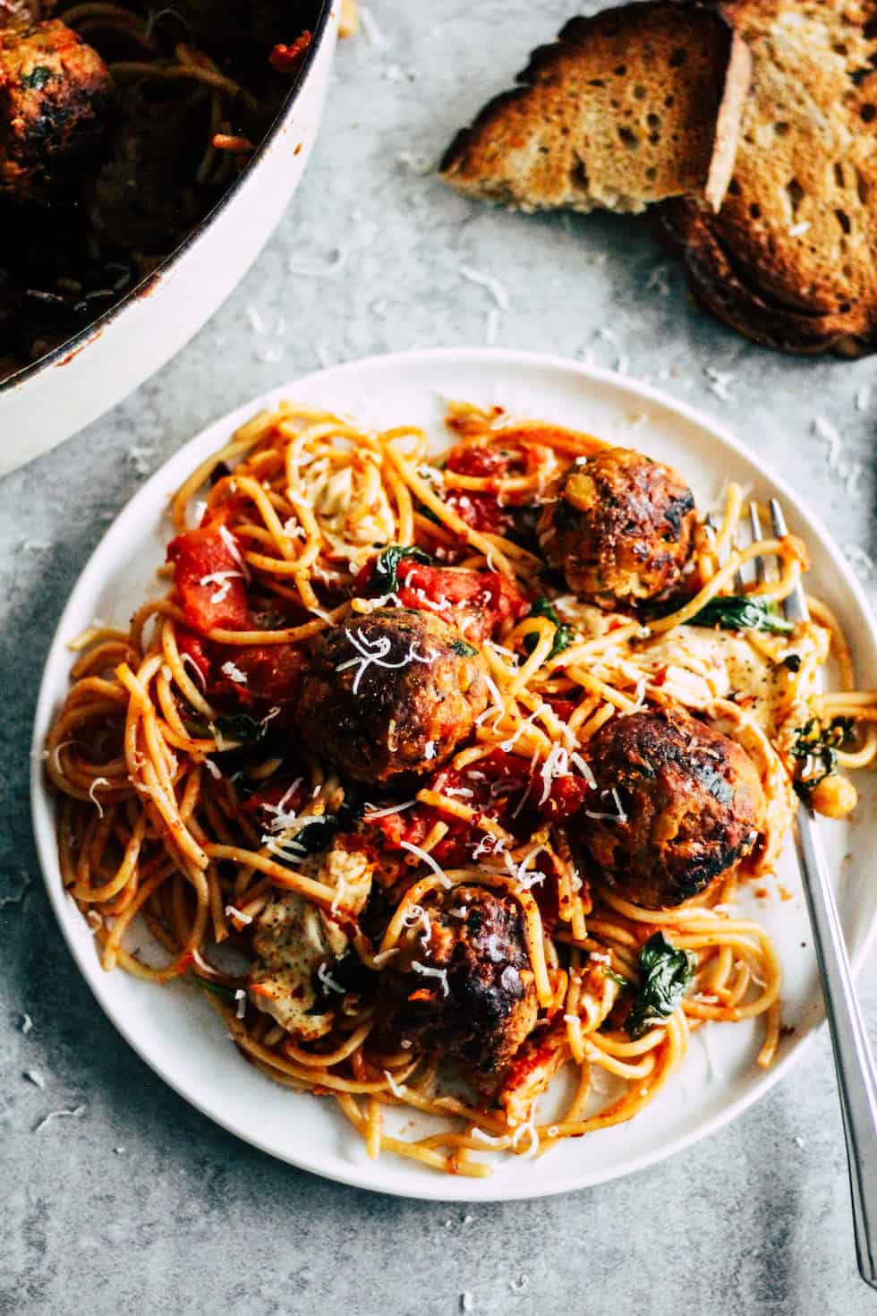 Spaghetti and meatballs on white plate with toasted bread in the background.