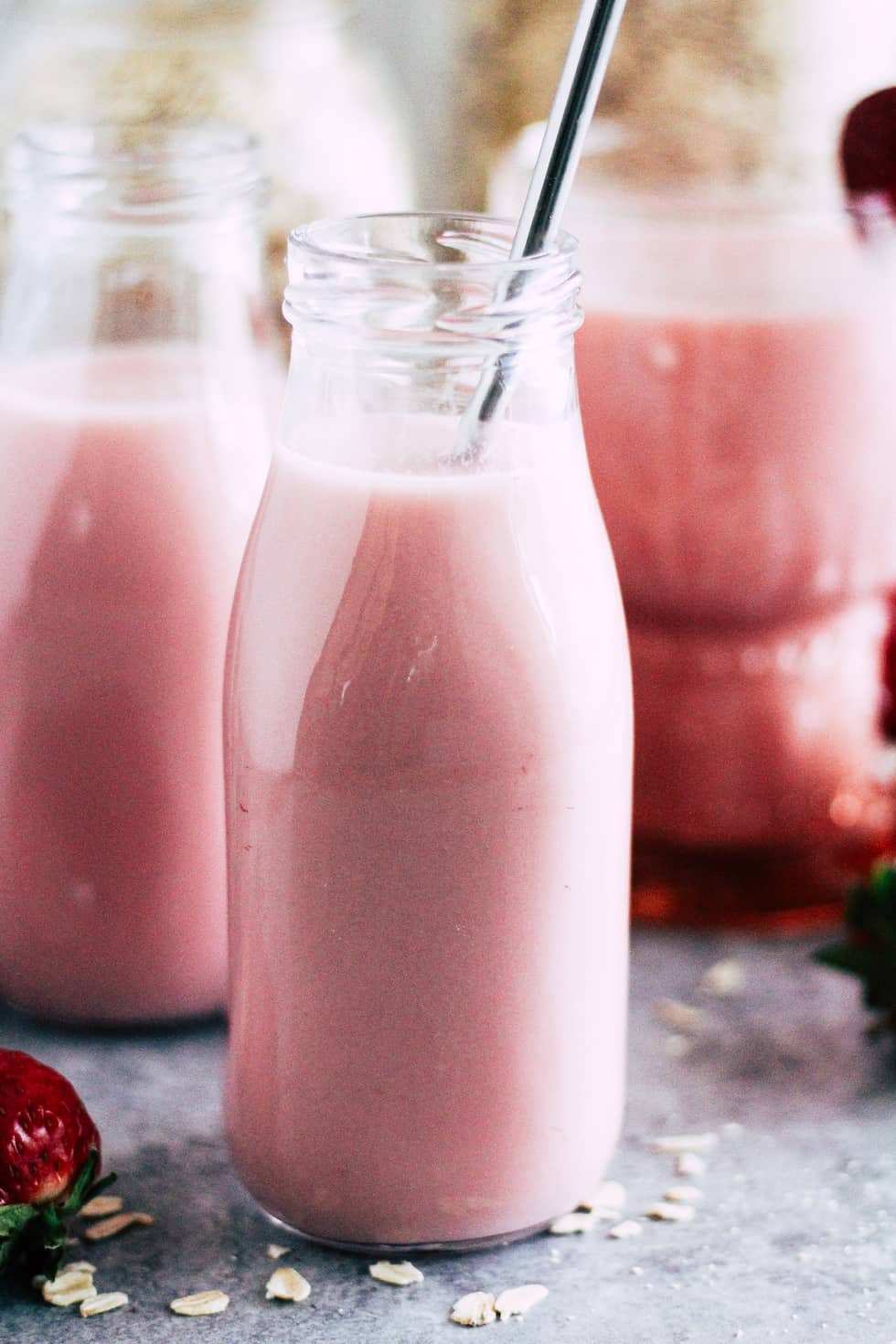 Milk jar filled with strawberry oat milk with a stainless steel straw.