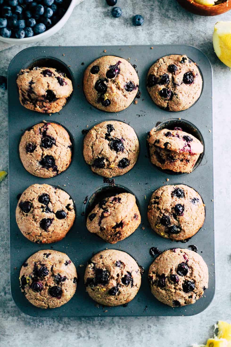 Muffin pan with whole wheat blueberry muffins and bowl of fresh blueberries.